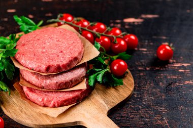 Raw burger with tomatoes and parsley. Against a dark background. High quality photo