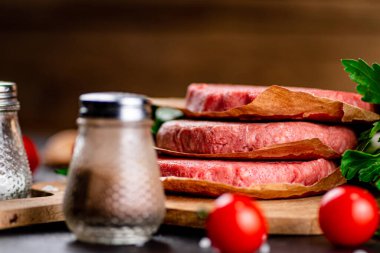 Raw burger with tomatoes and parsley. Against a dark background. High quality photo