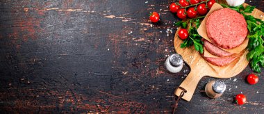 Raw burger with tomatoes and parsley. Against a dark background. High quality photo