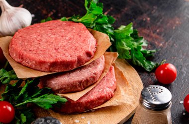 Raw burger on a wooden tray with tomatoes and dill. Against a dark background. High quality photo