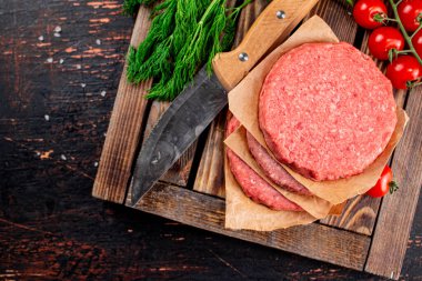 Raw burger on a wooden tray with tomatoes and dill. Against a dark background. High quality photo