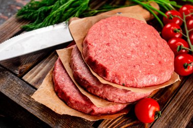 Raw burger on a wooden tray with tomatoes and dill. Against a dark background. High quality photo