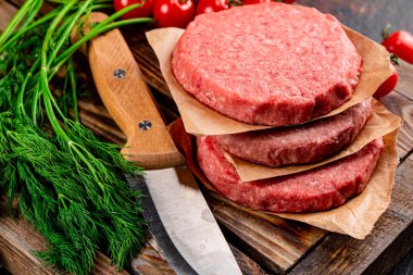 Raw burger on a wooden tray with tomatoes and dill. Against a dark background. High quality photo
