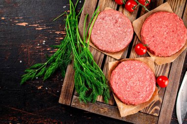 Raw burger on a wooden tray with tomatoes and dill. Against a dark background. High quality photo