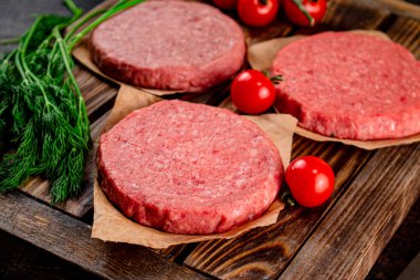 Raw burger on a wooden tray with tomatoes and dill. Against a dark background. High quality photo