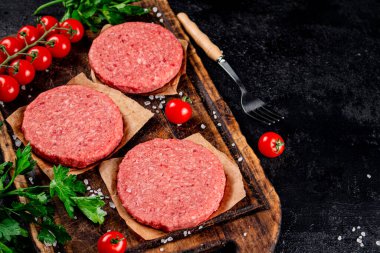 A raw burger on a tomato cutting board. On a black background. High quality photo