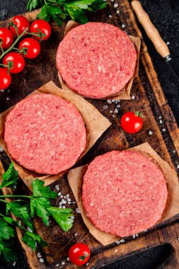 A raw burger on a tomato cutting board. On a black background. High quality photo