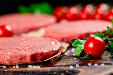 A raw burger on a tomato cutting board. On a black background. High quality photo
