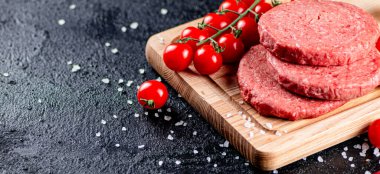 A raw burger on a tomato cutting board. On a black background. High quality photo