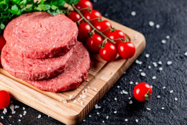 A raw burger on a tomato cutting board. On a black background. High quality photo