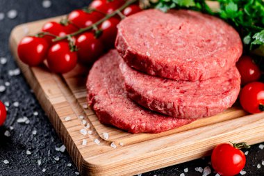 A raw burger on a tomato cutting board. On a black background. High quality photo