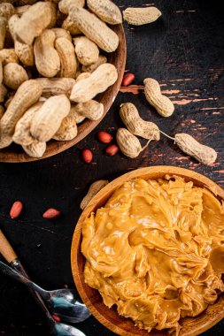 Peanut butter and inshell peanuts in wooden plates. On a rustic dark background. High quality photo