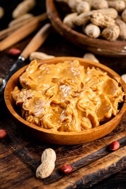 Peanut butter and inshell peanuts in wooden plates. On a rustic dark background. High quality photo