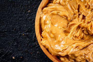 Peanut butter in a wooden plate on the table. On a black background. High quality photo