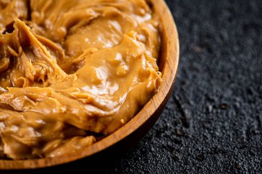 Peanut butter in a wooden plate on the table. On a black background. High quality photo