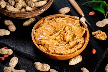 Peanut butter on a stone board with peanuts in the shell. On a black background. High quality photo
