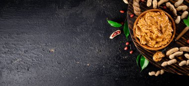 Peanut butter on a wooden tray with leaves. On a black background. High quality photo