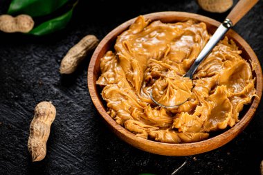 Peanut butter in a wooden plate. On a black background. High quality photo