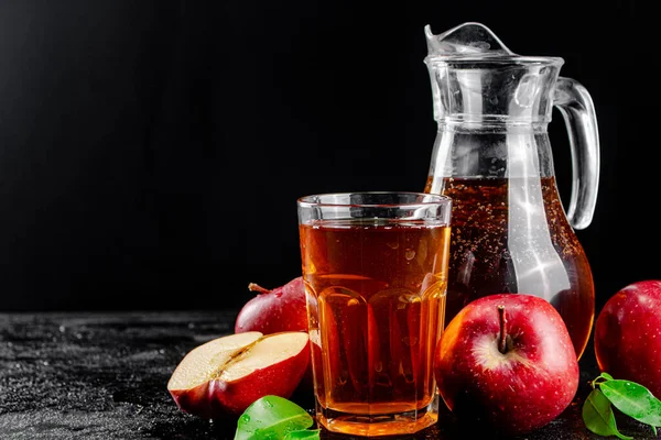 Apple juice in a jug and a glass on the table. On a black background. High quality photo