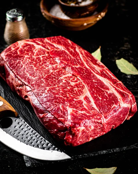 Raw beef on a stone board with a knife. On a black background. High quality photo