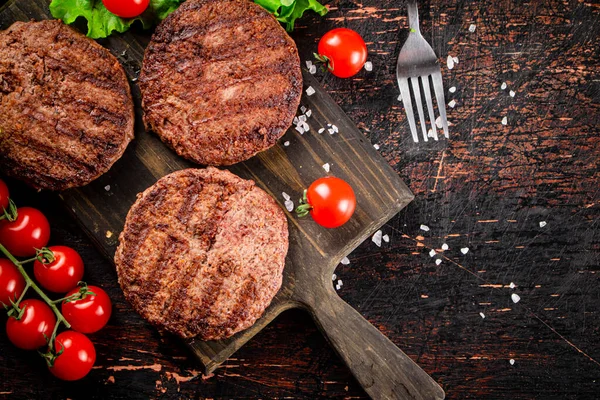 Stock image Burger grill on a cutting board with tomatoes and greens. On a rustic dark background. High quality photo