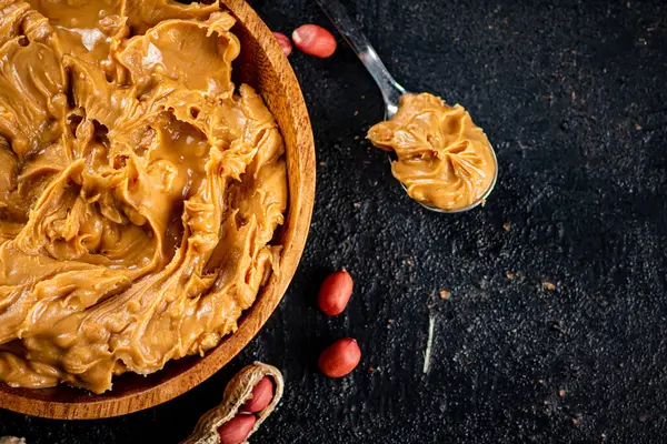 Peanut butter in a wooden plate on the table. On a black background. High quality photo