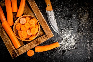 Whole and sliced carrots on a wooden tray. On a black background. High quality photo