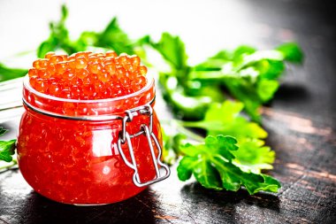 A full jar of red caviar with parsley on the table. On a rustic dark background. High quality photo