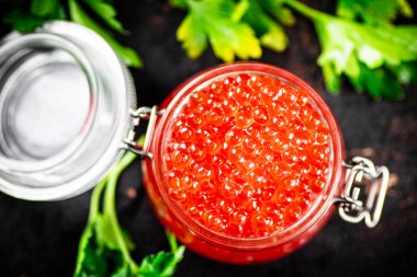 A full jar of red caviar with parsley on the table. On a rustic dark background. High quality photo