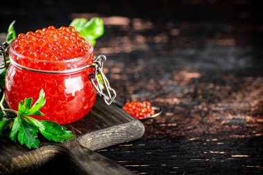 A full glass jar of red caviar on a cutting board. Against a dark background. High quality photo