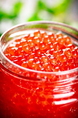 An open jar of red caviar with greens. On a rustic background. High quality photo