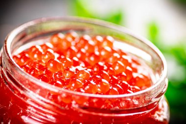 An open jar of red caviar with greens. On a rustic background. High quality photo