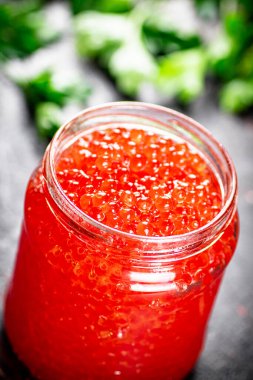 An open jar of red caviar with greens. On a rustic background. High quality photo