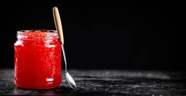 Red caviar in a glass jar on a table with a spoon. On a black background. High quality photo