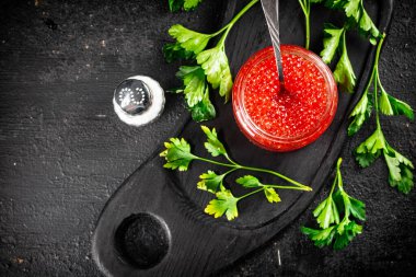 Red caviar in a glass jar with a spoon. On a black background. High quality photo