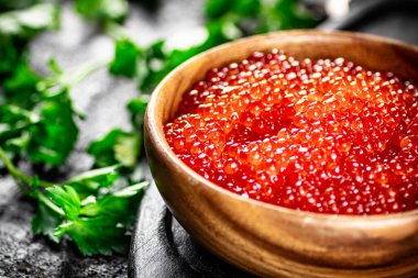 Red caviar in a plate on a cutting board with parsley. On a black background. High quality photo