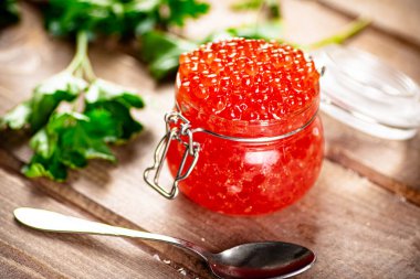 Red caviar in a glass jar with parsley. On a wooden background. High quality photo