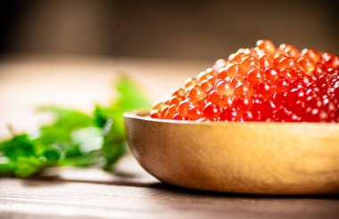 Red caviar in a plate on the table with parsley. On a wooden background. High quality photo