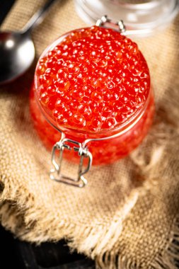 A glass jar with red caviar on burlap. On a black background. High quality photo