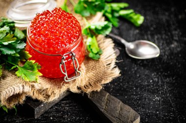 Red caviar on a cutting board with parsley. On a black background. High quality photo