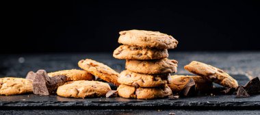 Cookies with pieces of milk chocolate on a stone board. On a black background. High quality photo