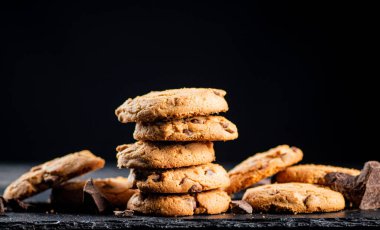 Cookies with pieces of milk chocolate on a stone board. On a black background. High quality photo