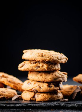 Cookies with pieces of milk chocolate on a stone board. On a black background. High quality photo