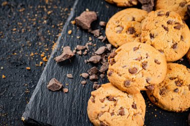 Cookies with pieces of milk chocolate on a stone board. On a black background. High quality photo