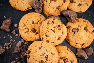 Cookies with pieces of milk chocolate on a stone board. On a black background. High quality photo
