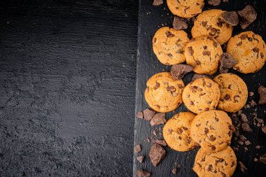 Cookies with pieces of milk chocolate on a stone board. On a black background. High quality photo