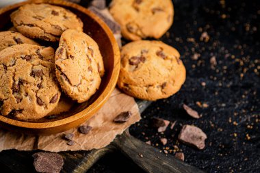 Cookies with pieces of milk chocolate on a cutting board. On a black background. High quality photo