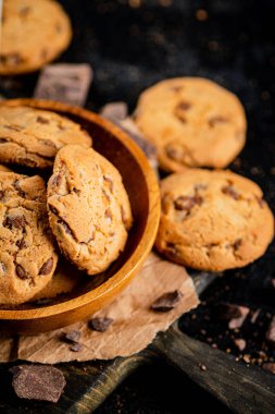 Cookies with pieces of milk chocolate on a cutting board. On a black background. High quality photo