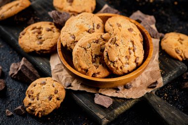 Cookies with pieces of milk chocolate on a cutting board. On a black background. High quality photo
