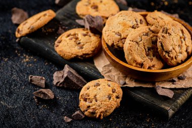 Cookies with pieces of milk chocolate on a cutting board. On a black background. High quality photo